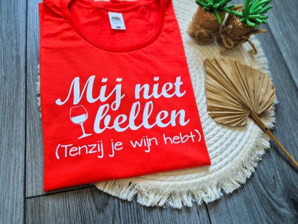 Detailfoto van Oranje t-shirt bedrukt met de tekst: Mij niet bellen (tenzij je wijn hebt). Het shirt is extra vrolijk dankzij het afgebeelde glas wijn.