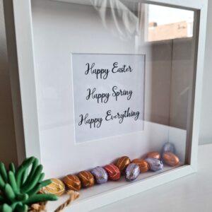 Houten witte fotolijst met de tekst: Happy Easter, Happy Spring, Happy Everything en gevuld met paaseieren