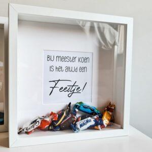 Houten witte fotolijst met de tekst: Bij meester / juf is het altijd een feestje. De lijst is gevuld met chocola.