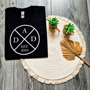 Zwart heren t-shirt bedrukt met een cirkel en de letters DAD. In het onderste vak staat het jaartal waarin de man vader is geworden. Dit wordt aangeduid met EST. 20..