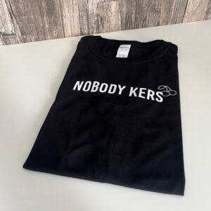 Zwart t-shirt bedrukt met grappige taalfout: Nobody Kers. Letterlijke vertaling van Nobody Cares.