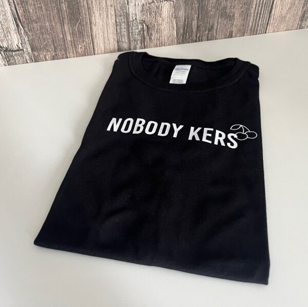 Zwart t-shirt bedrukt met grappige taalfout: Nobody Kers. Letterlijke vertaling van Nobody Cares.