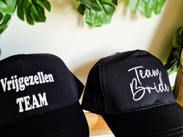 Detailfoto van zwarte petten bedrukt met de teksten 'vrijgezellen team' en 'team bride'