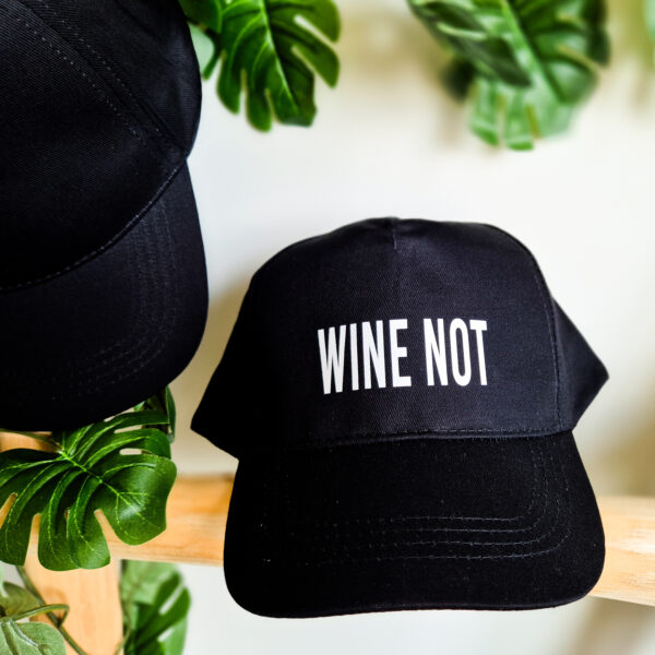 Detailfoto van zwarte, unisex pet bedrukt met de tekst 'Wine not'.