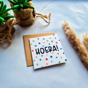 Een dubbelzijdige verjaardagskaart met de tekst Hoera. Geschreven in vrolijke handlettering en afgemaakt met kleurrijke stippen.